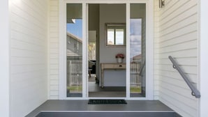 A front view of a house with a set of stairs leading to a door, a small porch area, and a window overlooking the backyard.