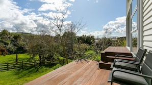 A wooden deck with outdoor seating, overlooking a grassy area with trees and a fence.