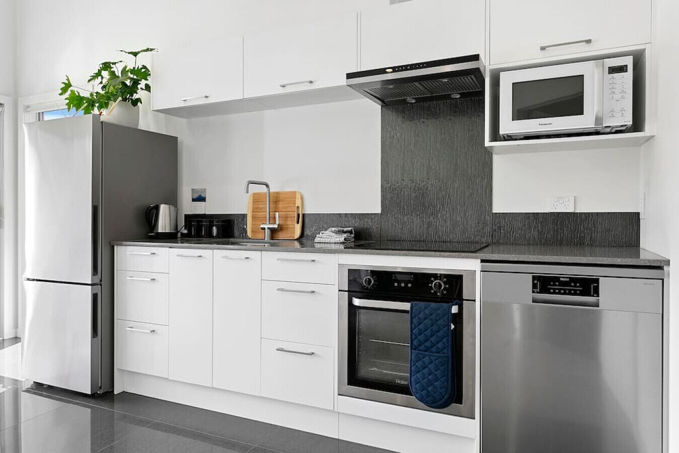 Een moderne keuken met witte kasten, roestvrijstalen apparatuur en een zwarte achterwand.