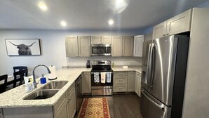 A modern kitchen with stainless steel appliances, granite countertops, and a patterned rug.