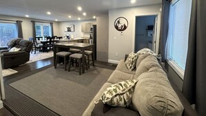 A modern living room with a sofa, a dining area, and a kitchen in the background.