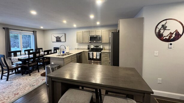A modern kitchen with built-in appliances, a dining area with a large table and chairs, and a view of the outdoors through a window.