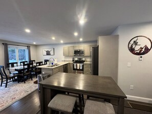 Een moderne keuken met inbouwapparatuur, een eethoek met een grote tafel en stoelen, en uitzicht op het buitenlands gebied door een raam.