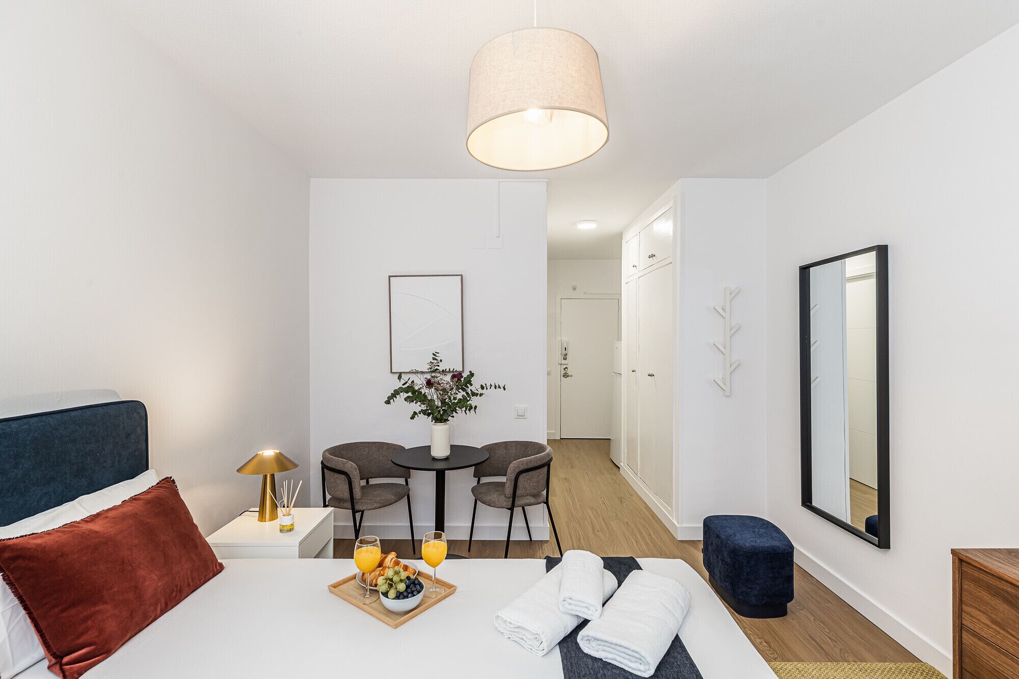 A modern hotel room with a bed, a dining area, and a bathroom.