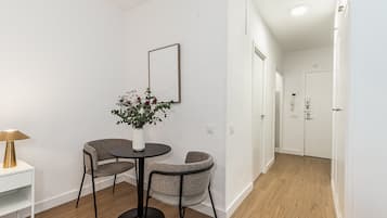 Een moderne, minimalistisch ingerichte kamer met een ronde tafel en twee stoelen, een klein wit tafeltje met een lamp en een vaas met bloemen.