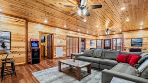 A spacious room with wooden walls and ceiling, a grey sofa, a coffee table, and a pool table. - Outdoor Theater + Jetted Hot Tub | 8BR Sleeps 24 (Sevierville)