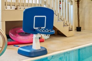 Un petit panier de basket d’intérieur, doté d’un panneau bleu et d’un cercle blanc, est placé sur une surface en bois, près d’une piscine.