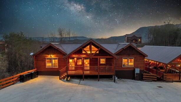A wooden cabin with multiple rooms, a porch, and a starry night sky. - Outdoor Theater + Jetted Hot Tub | 8BR Sleeps 24 (Sevierville)