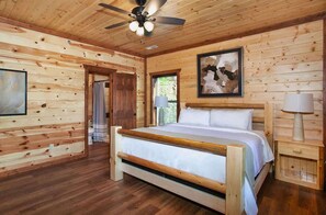 A wooden cabin bedroom with a bed, a ceiling fan, a framed picture, and a nightstand. - 8-Bedroom Cabin with Indoor Pool, Outdoor Theater & Hot Tub Near Dollywood (Sevierville)
