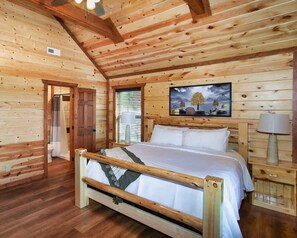 Une pièce de cabane en bois comprenant un lit, un tableau et une fenêtre avec des stores.