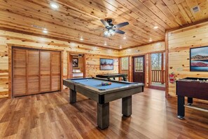 Un intérieur en bois avec une table de billard, un ventilateur de plafond et une table de baby-foot.
