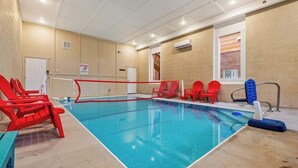 An indoor swimming pool with a volleyball net, red chairs, and a blue kickboard. - Outdoor Theater + Jetted Hot Tub | 8BR Sleeps 24 (Sevierville)
