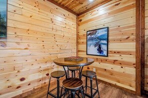 Ein Holzinterieur mit einem runden Tisch, Hockern, einem gerahmten Bild an der Wand und einem Holzboden.