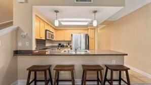 Una cocina moderna con una isla central, electrodomésticos de acero inoxidable y taburetes de madera.