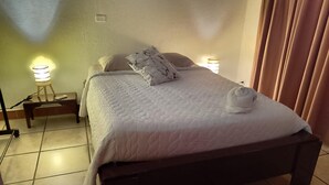 A neatly made bed with a white duvet and pillows, a bedside lamp, and a towel on the bed. - Family room 2 (Manuel Antonio)