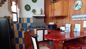 A kitchen with a red table, wooden cabinets, a microwave, and a coffee maker.