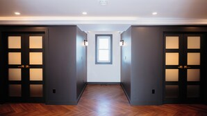 A hallway with dark walls, wooden flooring, and frosted glass doors.