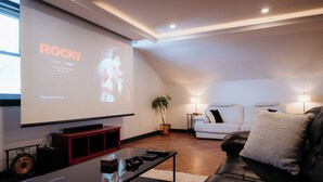 A modern living room with a large flat-screen TV, a black leather sofa, a white couch, and a wooden coffee table.