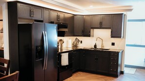 A modern kitchen with dark wood cabinets, a black refrigerator, and a wooden floor.