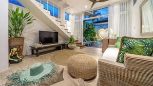 Una sala de estar moderna con un televisor grande, asientos cómodos, una escalera y ventanas amplias.