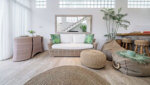 Una sala de estar moderna con sofá, reposapiés y mobiliario de mimbre, una escalera y un espejo grande.