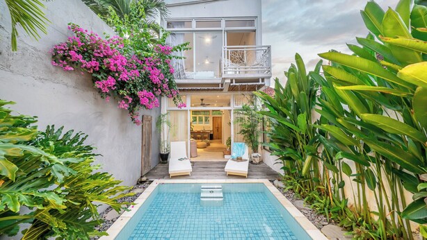 Una casa moderna con piscina, balcón y abundante vegetación.
