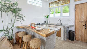 Una cocina moderna con una isla central, taburetes de bar, un lavamanos y un ventanal con vistas al verdor.