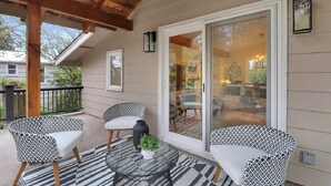 A covered patio with two patterned chairs, a glass table, and a potted plant.