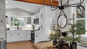 A modern kitchen with white cabinets, a wooden ceiling, and a dining area with a table set for two.