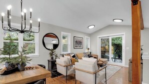 A spacious living room with a wooden dining table, two sofas, a chandelier, and large windows offering a view of the outdoors.