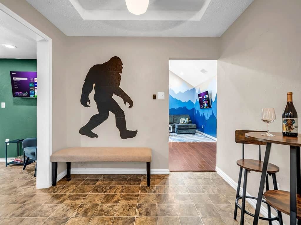A room with a large wall mural of a gorilla, a bench, a bar area with stools, and a TV mounted on the wall.