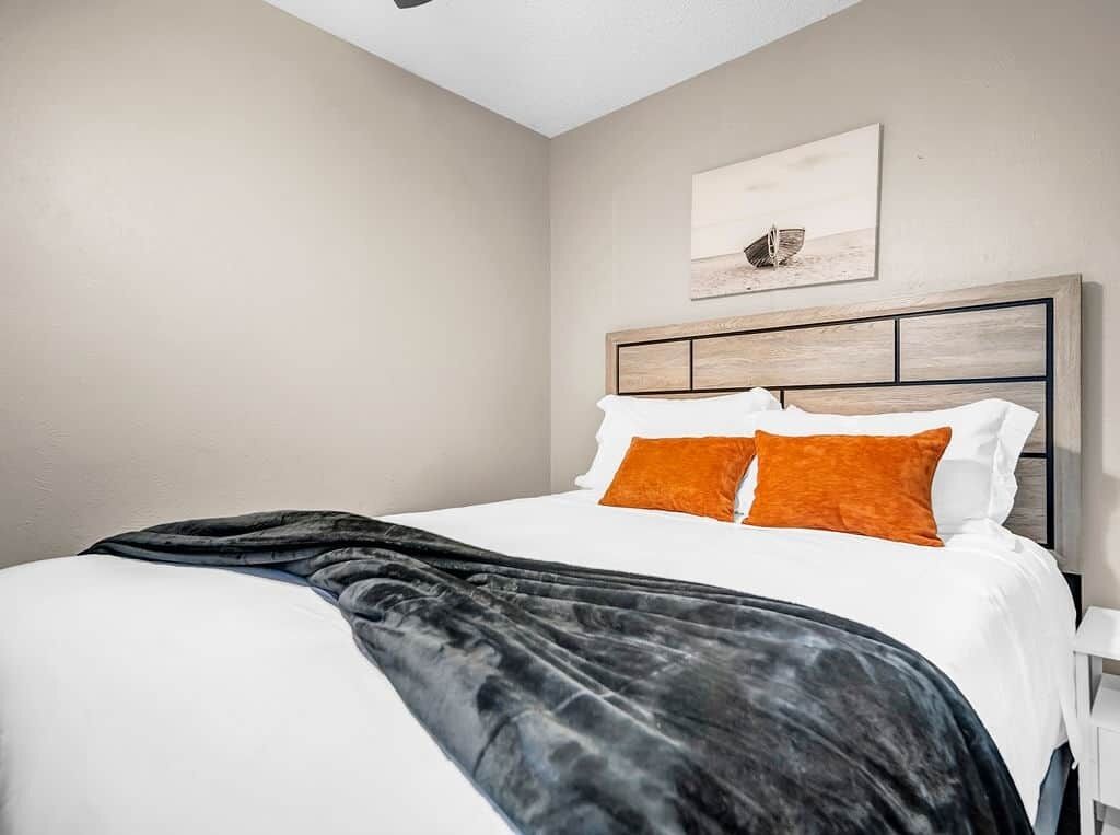 Una cama bien hecha con almohadas blancas y anaranjadas, una manta negra y un cabecero de madera.