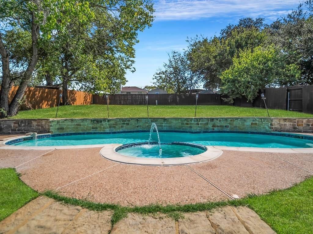 A backyard with a swimming pool, stone patio, and a wooden fence.