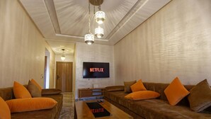 A living room with two brown sofas, a wooden coffee table, and a TV mounted on the wall. - Marrakech 2 Bedroom Brown Luxury Apartment (Marrakech)
