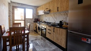 A kitchen with wooden cabinets, a stainless steel refrigerator, a washing machine, and a dining area with a table and chairs. - Marrakech 2 Bedroom Brown Luxury Apartment (Marrakech)