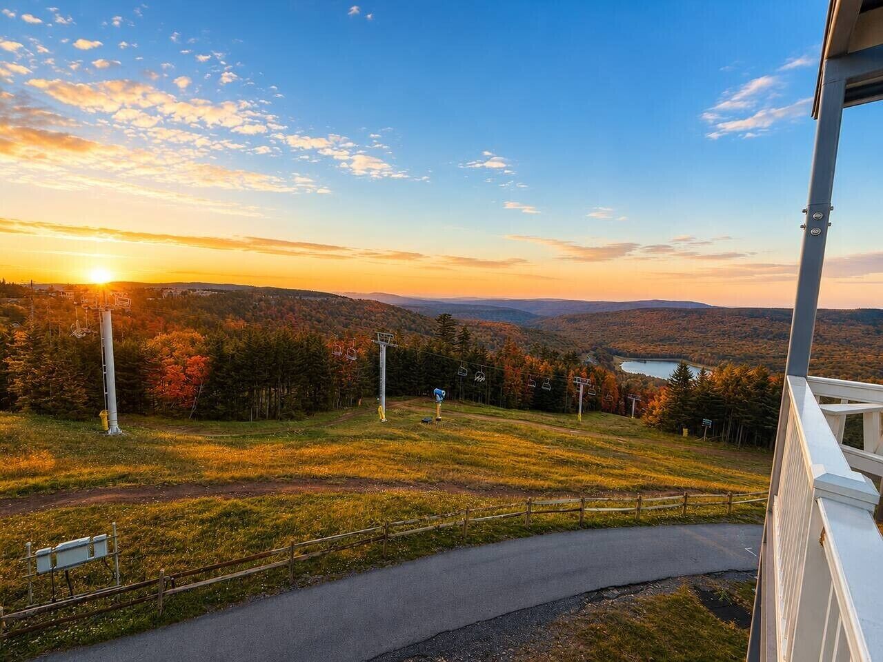 Une vue depuis une fenêtre donnant sur un paysage vallonné, avec une route, un télésiège et une étendue d'eau au loin.