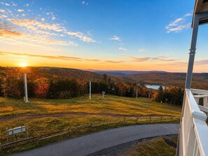 A view from a window overlooking a hilly landscape with a road, a ski lift, and a body of water in the distance.
