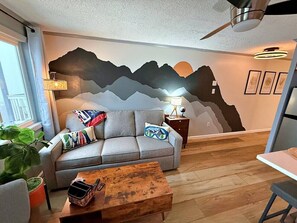 Un salon comprenant un canapé, une table basse, une lampe et une fresque murale.