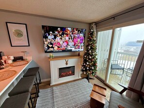 A living room with a fireplace, a TV, a Christmas tree, and a balcony with a view.