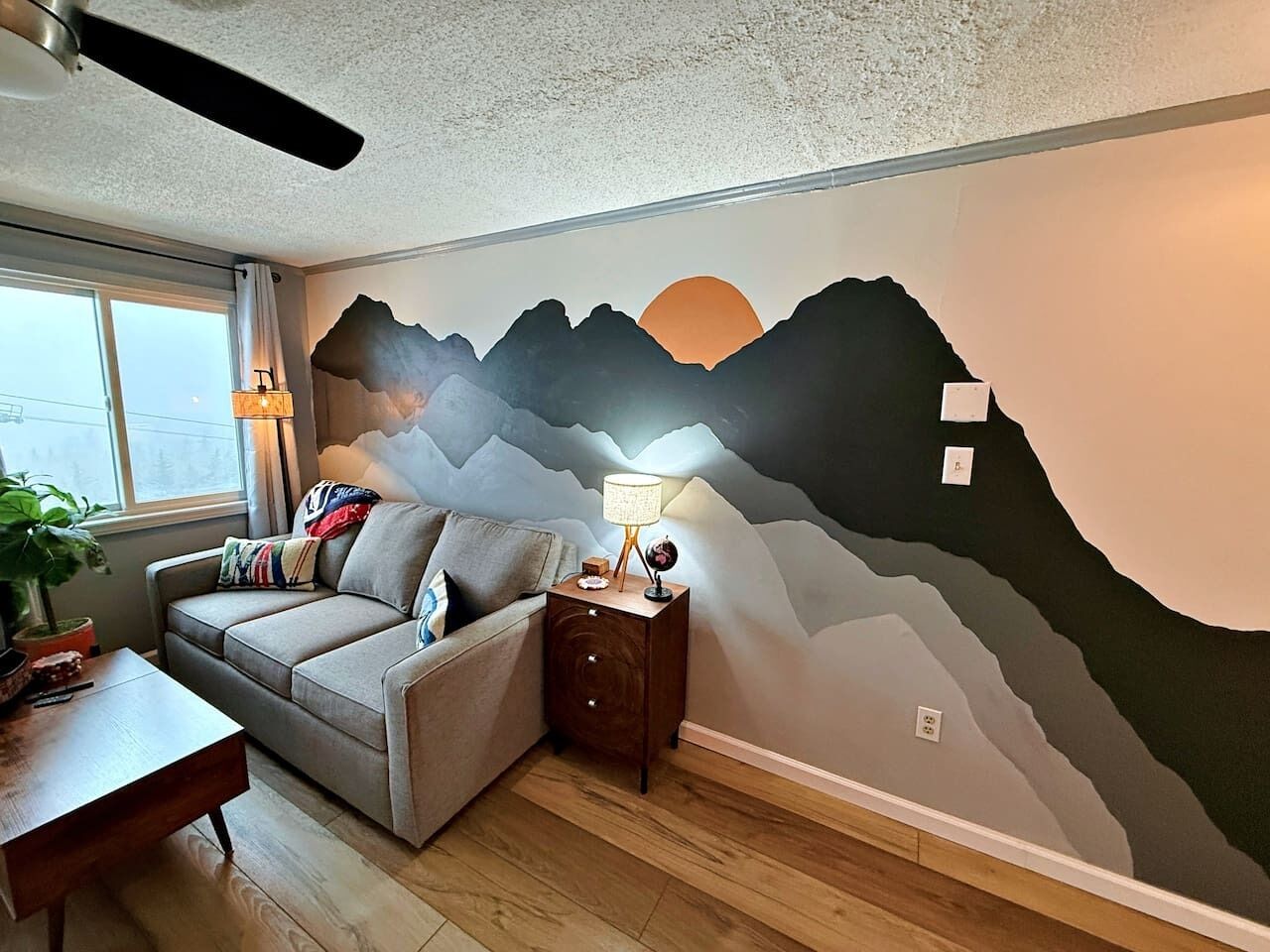 Un salon comprenant un canapé, une table d’appoint, une lampe et une fresque murale.