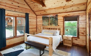 Ein Schlafzimmer einer Holzhütte mit Bett, Bank, Nachttisch und Fenstern.