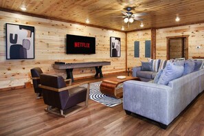 A wooden-paneled room with a sofa, chairs, a coffee table, a TV, and a ceiling fan. - 8-Bedroom Smoky Mountain Cabin with Indoor Pool, Theater & Game Room (Sevierville)