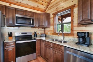 A kitchen with wooden cabinets, stainless steel appliances, granite countertops, and a window with a view. - 8-Bedroom Smoky Mountain Cabin with Indoor Pool, Theater & Game Room (Sevierville)