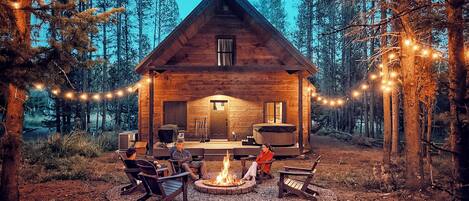 Una cabaña con un pozo de fuego, asientos exteriores y luces colgantes.