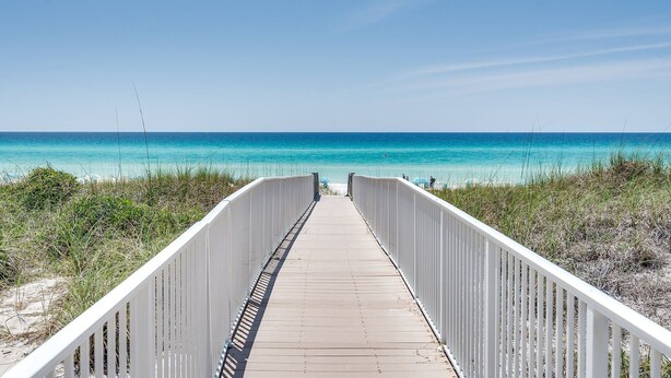 Une promenade en bois qui mène à une plage aux eaux d’un bleu limpide.