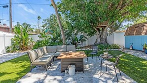 An outdoor patio with a wooden table, a sofa, and chairs. - Tangerine House | Fire pit + Tree House (Sarasota)