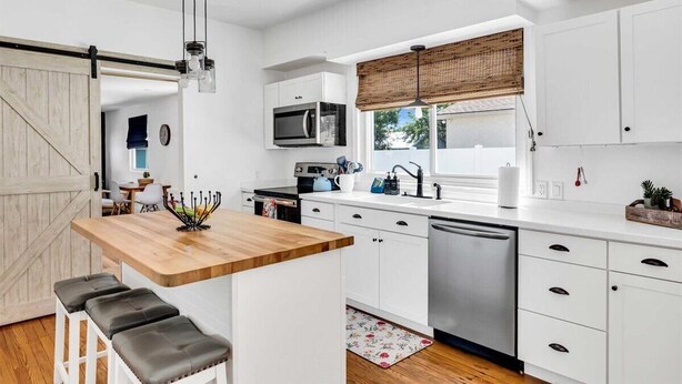 A modern kitchen with white cabinetry, a wooden island, and a dishwasher. - Tangerine House | Fire pit + Tree House (Sarasota)