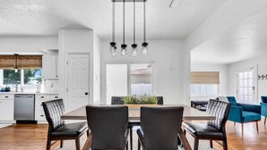 A spacious living room with a dining area, featuring a large wooden table, dark leather chairs, and a modern chandelier. - Tangerine House | Fire pit + Tree House (Sarasota)