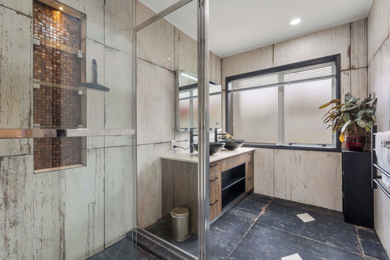 A modern bathroom with a glass shower enclosure, a wooden vanity, and a large window providing natural light.