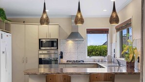 Una cocina moderna con una isla central, electrodomésticos de acero inoxidable, iluminación colgante y vistas a través de un ventanal.